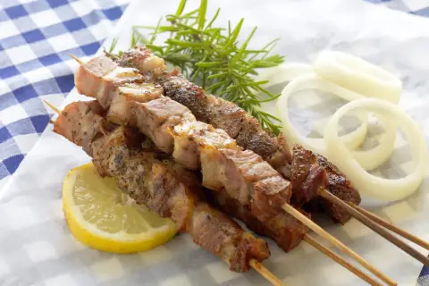 Aromatyczne souvlaki na patyczkach, podane z plasterkiem cytryny, gałązką rozmarynu i krążkami cebuli.