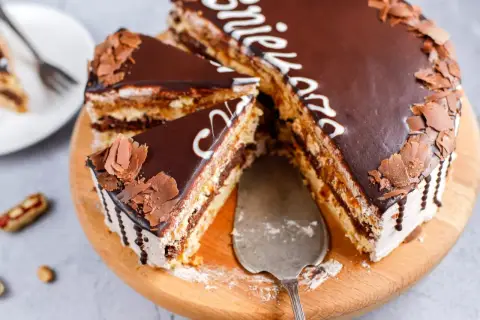 Pyszny tort snickers z czekoladą i orzeszkami, pokrojony na kawałki, gotowy do podania.