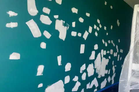 Ściana w trakcie malowania, białe plamy na turkusowym tle. Szacowany koszt malowania mieszkania 50 m.