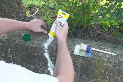 Hände dichten Betonrisse mit einer Tube ab. Ein Spachtel und Pinsel liegen bereit.