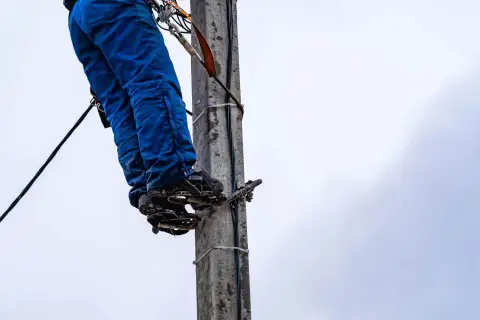 Energetyka chce zakopać kabel na mojej działce. Pracownik na słupie w niebieskich spodniach i z przyrządami.