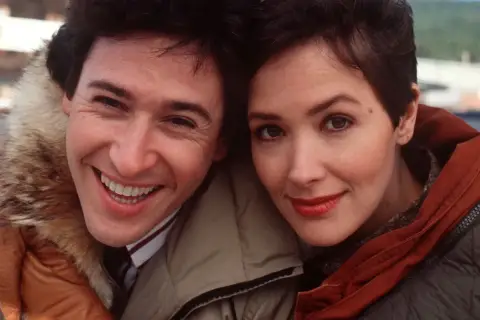 Uśmiechnięci John Cusack i Annette Bening, główni bohaterowie filmu "Przystanek Alaska", w zimowych kurtkach.