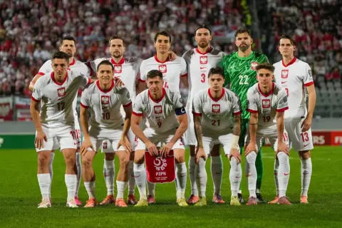 Zgrupowanie reprezentacji Polski. Piłkarze w białych strojach z orłem na piersiach pozują na tle trybun.