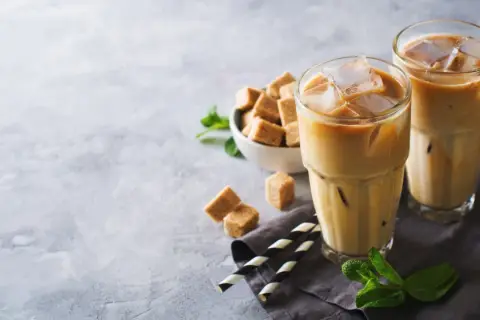 Dwa orzeźwiające freddo espresso z lodem, kostki brązowego cukru i listki mięty na szarym tle. Idealne na upalny dzień.