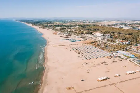 Vue aérienne d'une longue plage de sable fin bordée par la mer bleue, avec des rangées de parasols et des bâtiments à Catane, Sicile.