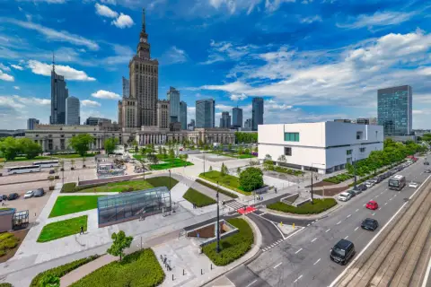 Warszawski plac defilad z Pałacem Kultury i Nauki, nowoczesnym budynkiem i ruchliwą ulicą.