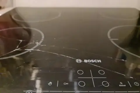 Pęknięta płyta indukcyjna Bosch z widocznymi rysami i pęknięciami na szkle.