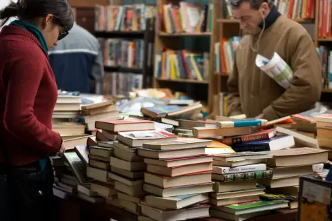 Stapel von Büchern in einem Antiquariat. Eine Frau und ein Mann suchen nach historischen Romanen, die auf wahren Begebenheiten basieren.