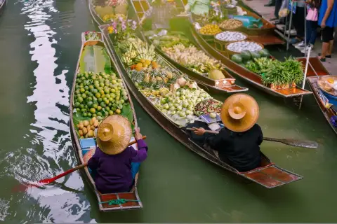 Bunte Boote voller Früchte und Gemüse auf einem **floating market**. Händler mit traditionellen Hüten rudern durch das Wasser.