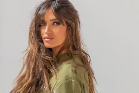 Mujer con cabello castaño largo y ondulado, con flequillo cortina que enmarca su rostro.