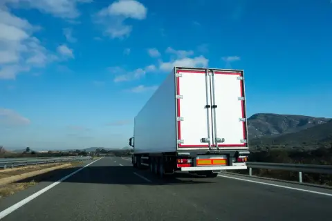 Biała naczepa ciężarówki na autostradzie, przewożąca fracht. Co to jest fracht? To towar w transporcie.