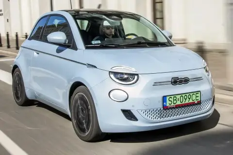 Jasnoniebieski fiat elektryczny 500 z czarnym dachem jedzie ulicą. Kierowca w okularach przeciwsłonecznych prowadzi auto.
