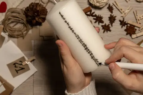 Hände beschriften eine Kerze mit Zahlen für einen Adventskalender. So lassen sich Adventskalender Geschenke selber machen.
