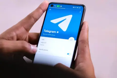 Dłonie trzymają smartfon z otwartą aplikacją Telegram. Widać logo i opcje powiadomień, idealne do dyskretnych rozmów w tajnych grupach Telegram.