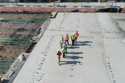 Grupa budowlańców na placu budowy. Widać zbrojenie i świeży beton. Sprawdzają beton b25 cena za m3.