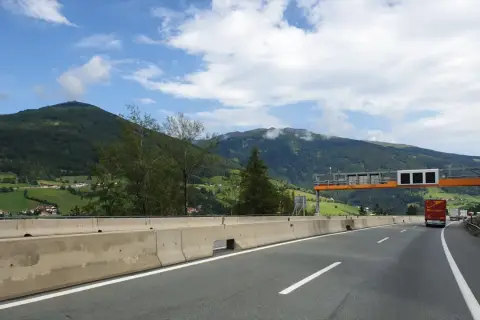 Autostrada w Austrii z widokiem na góry, znaki drogowe i ciężarówka.