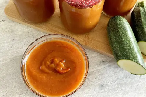 Domowy ketchup z cukinii siostry Anastazji w słoikach i miseczce, obok świeże cukinie.