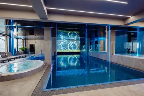 Nowoczesny basen i jacuzzi w rezydencji Aqua Szklarska Poręba. Niebieskie podświetlenie i ekran z animacją tworzą relaksującą atmosferę.