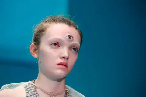Modelka z trzecim okiem na czole, jakby otwierała się jej szyszynka. Jasna skóra, białe brwi, niebieskie oczy.