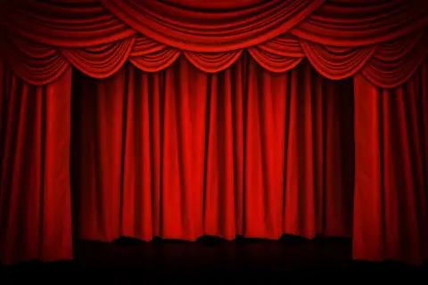 Czerwona, teatralna kurtyna w teatrze, z bogatymi drapowaniami u góry, gotowa do odsłonięcia sceny.