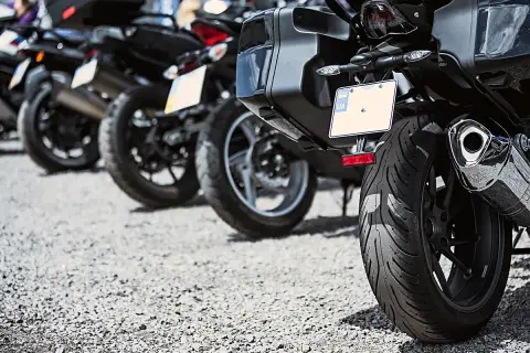 Varias motos aparcadas en fila, una moto sin matrícula visible en primer plano, con su rueda trasera y maleta.
