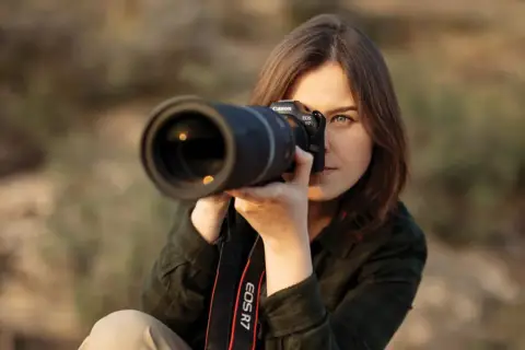 Kobieta z aparatem Canon EOS R7, skupiona na kadrze. Dopasowuje ustawienia aparatu, by uchwycić idealny moment.
