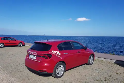 Czerwony fiat tipo sedan zaparkowany nad błękitnym jeziorem.