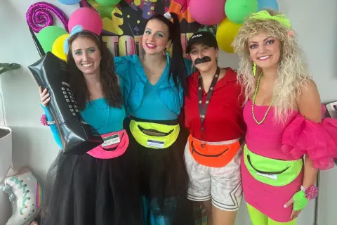Cuatro amigas celebran una fiesta moda de los 80 con atuendos coloridos, riñoneras y peinados voluminosos.