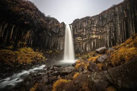Svartifoss, najpiękniejszy wodospad, spada kaskadą wśród bazaltowych kolumn. Otoczenie skaliste i jesienna roślinność tworzą magiczny krajobraz.