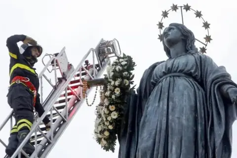 Vigile del fuoco su scala decora la statua della Madonna con fiori per l'8 dicembre a Roma.