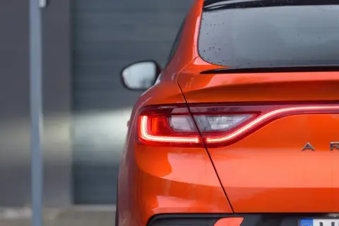 Pomarańczowy Renault Arkana z włączonymi światłami LED. Zbliżenie na tylną część auta, gdzie widoczne są detale nadwozia i nazwa modelu. Idealne wymiary dla miejskiej dżungli.
