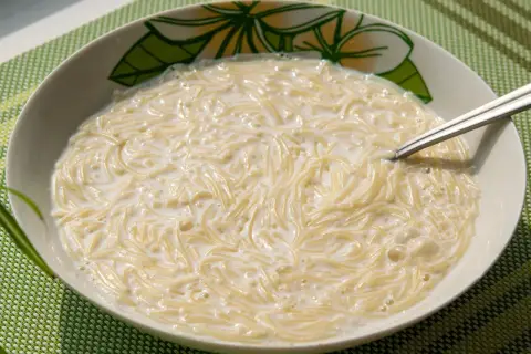 Zupa mleczna z makaronem, podana w misce z motywem kwiatowym. Widoczna łyżeczka zanurzona w kremowym daniu.