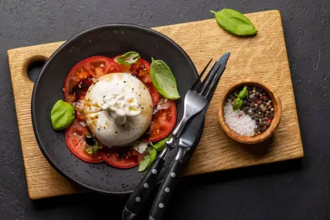 Ser burrata z pomidorami i bazylią. Idealny sposób, jak jeść burratę: z pieprzem, solą i oliwą.