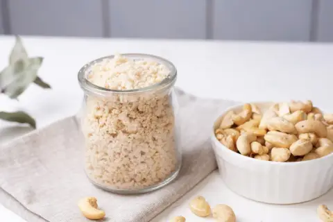 Zutaten für veganen Parmesan selber machen: Cashewkerne in einer Schüssel und fertig gemahlene Masse in einem Glas.