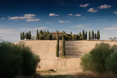 Dom toscano immerso nel verde, un sogno di agriturismo in Italia. Cipressi e campi dorati sotto un cielo azzurro.