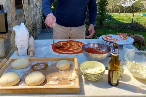 Przygotowanie pizzy w słonecznym Chianti, Włochy. Ciasto, sos pomidorowy i ser czekają na pieczenie.
