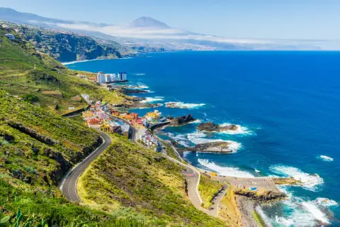 Costa de Tenerife con pueblo colorido, mar azul y el Teide al fondo. ¡Perfecto para tus viajes a Tenerife todo incluido 2x1!