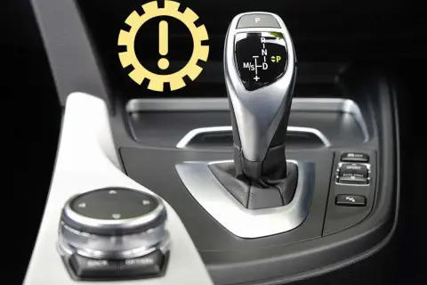 Awaryjne odblokowanie skrzyni biegów w BMW. Ikona ostrzeżenia nad dźwignią zmiany biegów.