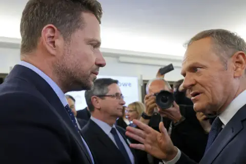 Czy Donald Tusk rzeczywiście obawia się ambicji prezydenckich Rafała Trzaskowskiego? Politycy rozmawiają w tłumie, w tle dziennikarze z aparatami.