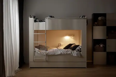 Przytulny mały pokój z łóżkiem piętrowym, idealnym dla dzieci. Na dolnym łóżku pluszowy miś i poduszki czekają na nocne opowieści.