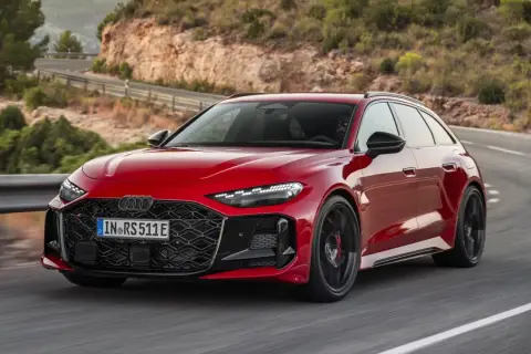 Czerwone, nowe RS5 Avant sunie po krętej drodze w górach.