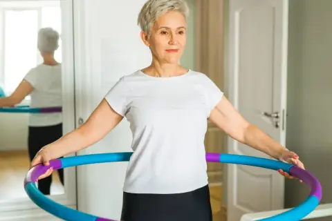 Kobieta w białej koszulce ćwiczy z kolorowym hula hop.