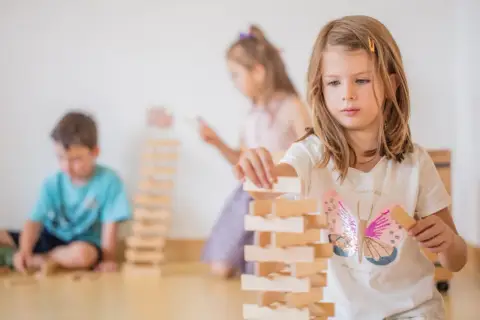 Kinder bauen in der Bauecke im Kindergarten einen hohen Turm aus Holzklötzen.