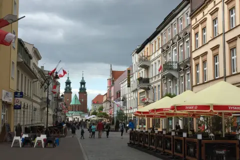 Spacer po Gnieźnie, gdzie widać zabytkowe kamienice, katedrę i ludzi odpoczywających w ogródku piwnym.