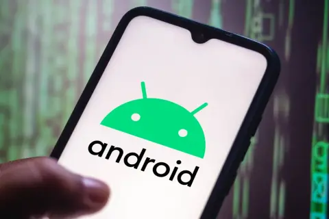 Dłoń trzyma smartfon z logo Android 10. W tle widać zielony, cyfrowy kod.