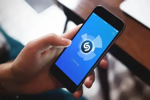Dłoń trzyma smartfon z aplikacją Shazam, która analizuje dźwięk. Zastanawiasz się, jaka to piosenka?