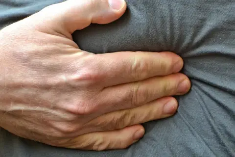 Eine Hand drückt auf den Bauch, was auf Beschwerden wie bei einer Lebensmittelunverträglichkeit hindeuten könnte.
