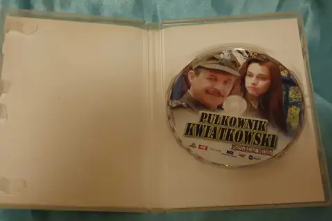 Płyta DVD z filmem "Pułkownik Kwiatkowski" i jego obsadą. Widoczni są główni bohaterowie, pułkownik i młoda kobieta.