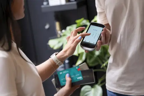 Kobieta wpisuje kod PIN na telefonie, trzymając kartę Visa. Czy płatność kartą w internecie jest bezpieczna? Tak, dzięki nowoczesnym zabezpieczeniom.