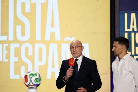 Mężczyzna w garniturze z mikrofonem i piłkarze Hiszpanii na tle napisu "LISTA DE ESPAÑA".